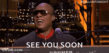 A Man Wearing Sunglasses Is Singing Into A Microphone And Saying `` See You Soon '' While Playing A Keyboard . GIF
