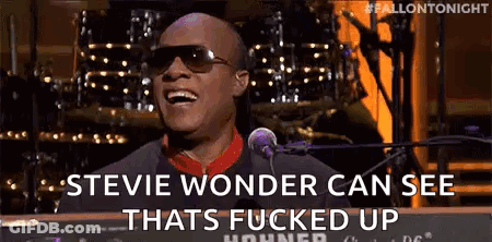 A Man Wearing Sunglasses Is Singing Into A Microphone While Playing A Keyboard . GIF