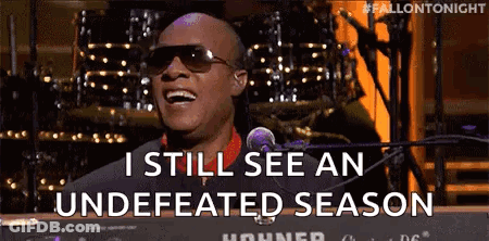 A Man Wearing Sunglasses Is Singing Into A Microphone While Sitting At A Keyboard . GIF