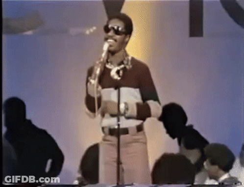 A Man Wearing Sunglasses Is Singing Into A Microphone While Standing In Front Of A Crowd . GIF