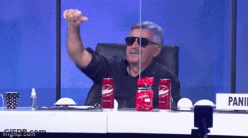 A Man Wearing Sunglasses Is Sitting At A Table With Two Red Cans Of Budweiser GIF