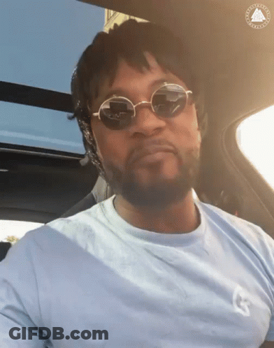 A Man Wearing Sunglasses Is Sitting In A Car With The Letter G On His Shirt GIF
