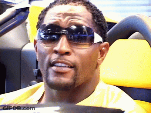 A Man Wearing Sunglasses Is Sitting In A Yellow Vehicle GIF