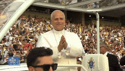 A Man Wearing Sunglasses Is Sitting In Front Of A Crowd With A Sign That Says ' Rio 2016 ' On It GIF