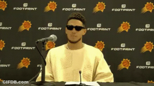 A Man Wearing Sunglasses Is Sitting In Front Of A Footprint Banner GIF