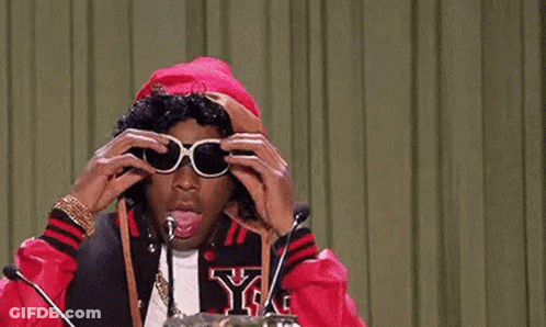 A Man Wearing Sunglasses Is Sitting In Front Of A Microphone And Talking Into It . GIF