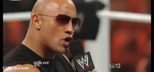 A Man Wearing Sunglasses Is Speaking Into A Microphone With The Word Wwe On It GIF