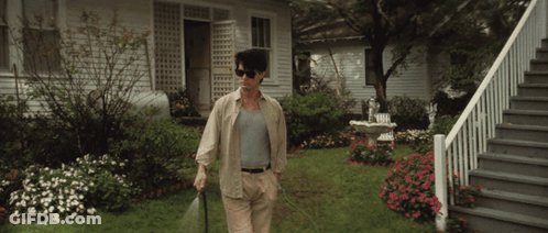 A Man Wearing Sunglasses Is Spraying The Grass In Front Of A House GIF