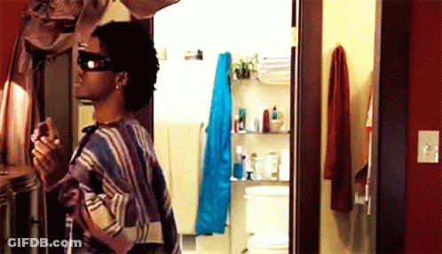 A Man Wearing Sunglasses Is Standing In A Bathroom GIF