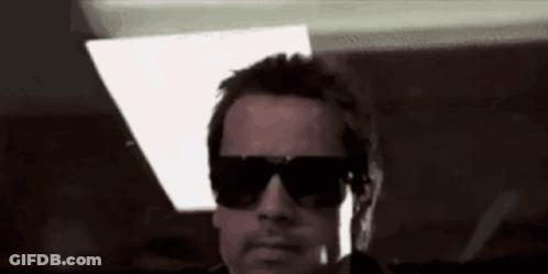A Man Wearing Sunglasses Is Standing In A Dark Room . GIF