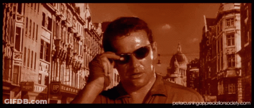 A Man Wearing Sunglasses Is Standing In Front Of A Building That Says Bp Platters GIF