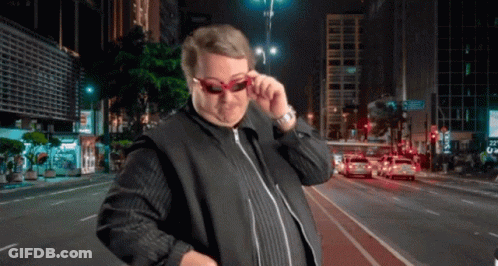 A Man Wearing Sunglasses Is Standing In Front Of A City Street At Night GIF
