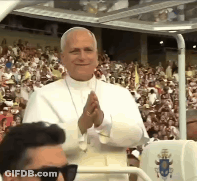 A Man Wearing Sunglasses Is Standing In Front Of A Crowd Of People Applauding The Pope . GIF
