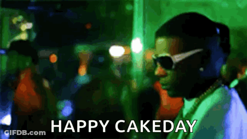 A Man Wearing Sunglasses Is Standing In Front Of A Crowd With The Words Happy Cakeday Written Below Him . GIF