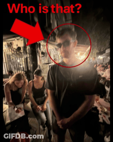 A Man Wearing Sunglasses Is Standing In Front Of A Group Of People With A Red Arrow Pointing To The Man 'S Face GIF
