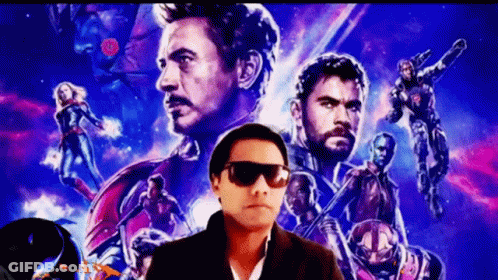 A Man Wearing Sunglasses Is Standing In Front Of A Movie Poster For The Avengers GIF