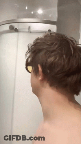 A Man Wearing Sunglasses Is Standing In Front Of A Shower GIF