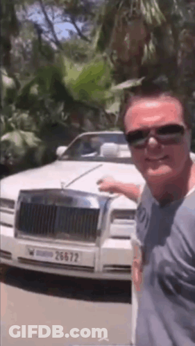 A Man Wearing Sunglasses Is Standing In Front Of A White Rolls Royce . GIF