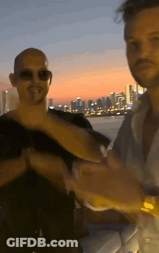 A Man Wearing Sunglasses Is Standing Next To Another Man GIF