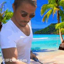 A Man Wearing Sunglasses Is Standing On A Beach With A Knife GIF