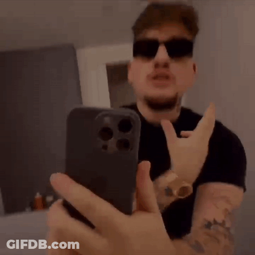 A Man Wearing Sunglasses Is Taking A Selfie With His Mouth Open While Holding A Cell Phone . GIF