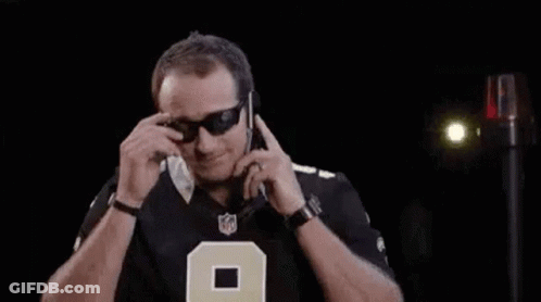 A Man Wearing Sunglasses Is Talking On A Cell Phone In A Dark Room . GIF