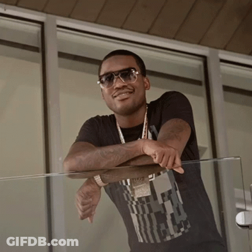 A Man Wearing Sunglasses Leans On A Glass Railing With His Arm Resting On His Elbow GIF