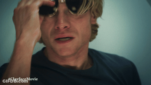 A Man Wearing Sunglasses Looks Through Binoculars With #Clayfacemovie Written Below Him GIF