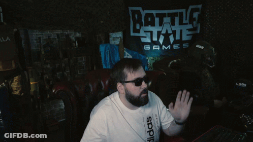 A Man Wearing Sunglasses Sits In Front Of A Battle State Games Sign GIF
