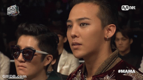 A Man Wearing Sunglasses Sits Next To A Man Wearing A Jacket With The Word Mama Written On It GIF