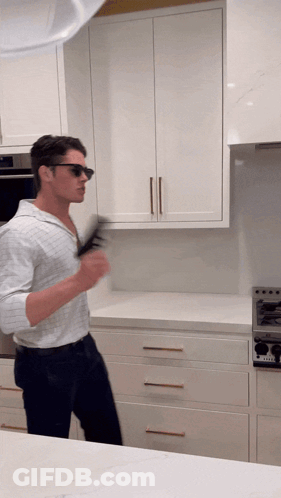 A Man Wearing Sunglasses Stands In A Kitchen With White Cabinets GIF