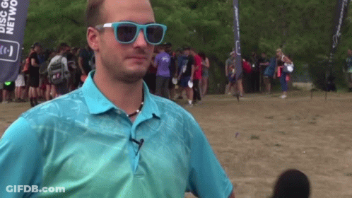 A Man Wearing Sunglasses Stands In Front Of A Banner That Says Disc Golf GIF