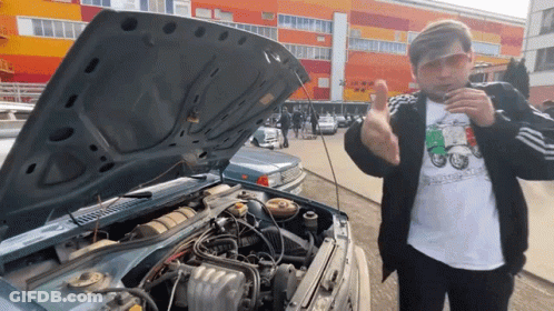 A Man Wearing Sunglasses Stands In Front Of A Car With The Hood Open And The Engine Exposed GIF