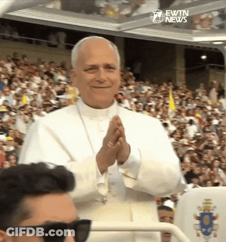 A Man Wearing Sunglasses Stands In Front Of A Crowd With Ewtn News Written On The Bottom Right GIF