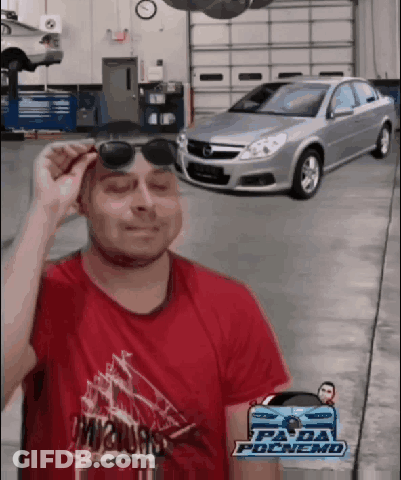 A Man Wearing Sunglasses Stands In Front Of A Garage Door With A Car In The Background GIF