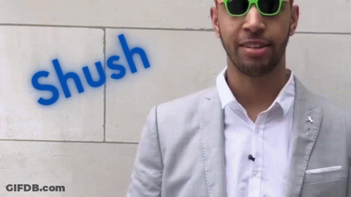 A Man Wearing Sunglasses Stands In Front Of A Wall That Has The Word Shush Painted On It GIF