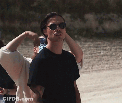 A Man Wearing Sunglasses Stands In Front Of A Woman GIF