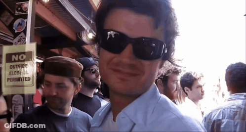 A Man Wearing Sunglasses Stands Next To A Sign That Says No Outside Alcohol Permitted GIF