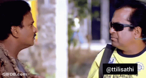 A Man Wearing Sunglasses Talks To Another Man In A Yellow Shirt That Says ' Ttilisathi ' On It GIF