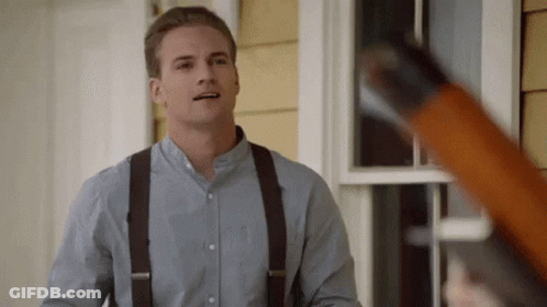 A Man Wearing Suspenders And A Blue Shirt Is Standing In Front Of A House Holding A Shotgun . GIF