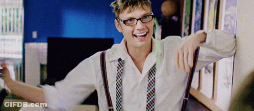 A Man Wearing Suspenders And Glasses Is Smiling And Leaning Against A Wall GIF