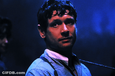 A Man Wearing Suspenders Looks At The Camera With A Blue Background GIF