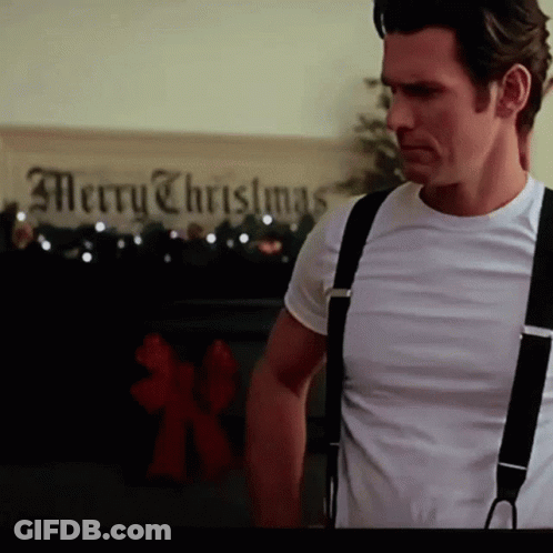 A Man Wearing Suspenders Stands In Front Of A Merry Christmas Sign GIF