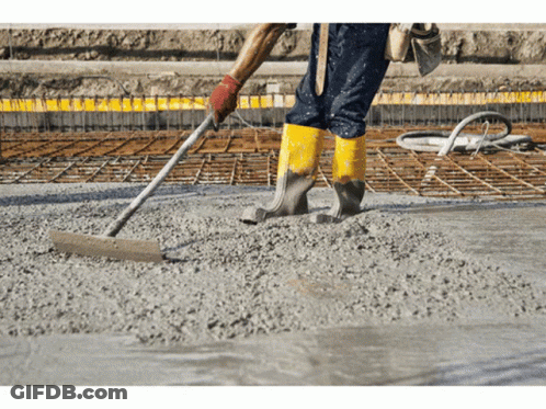 A Man Wearing Yellow Boots Is Raking Concrete On A Construction Site GIF