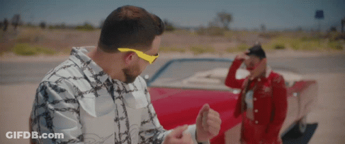 A Man Wearing Yellow Sunglasses Stands Next To A Woman In A Red Dress GIF