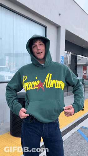 A Man Wears A Green Hoodie That Says Gracie Abram GIF