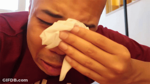 A Man Wipes His Nose With A Tissue While Wearing A Maroon Shirt With The Letter H On It GIF