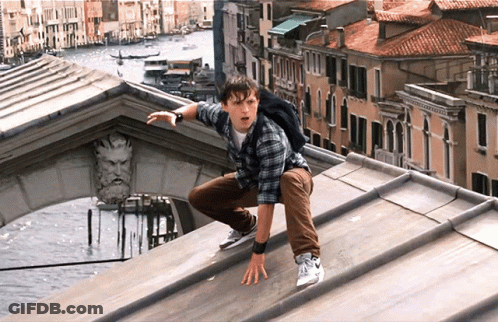 A Man With A Backpack Is Crawling On The Roof Of A Building Overlooking A City GIF