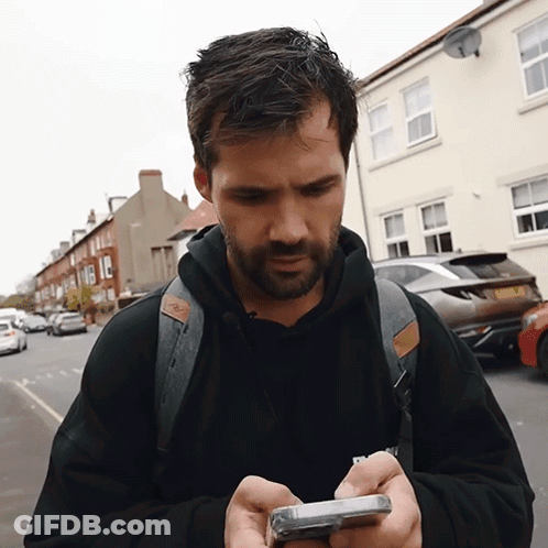 A Man With A Backpack Is Looking At His Cellphone GIF