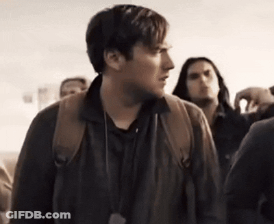 A Man With A Backpack Is Standing In A Crowd Of People And Looking At The Camera . GIF
